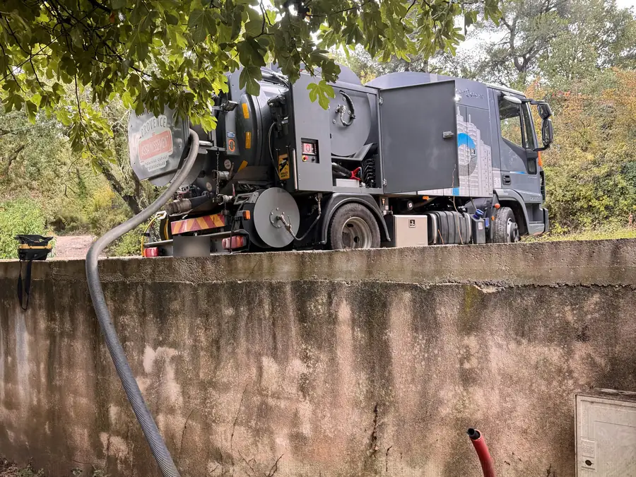 Le camion de Provence Assainissement en intervention, garé au-dessus d'un mur, un tuyau qui descend dans le jardin