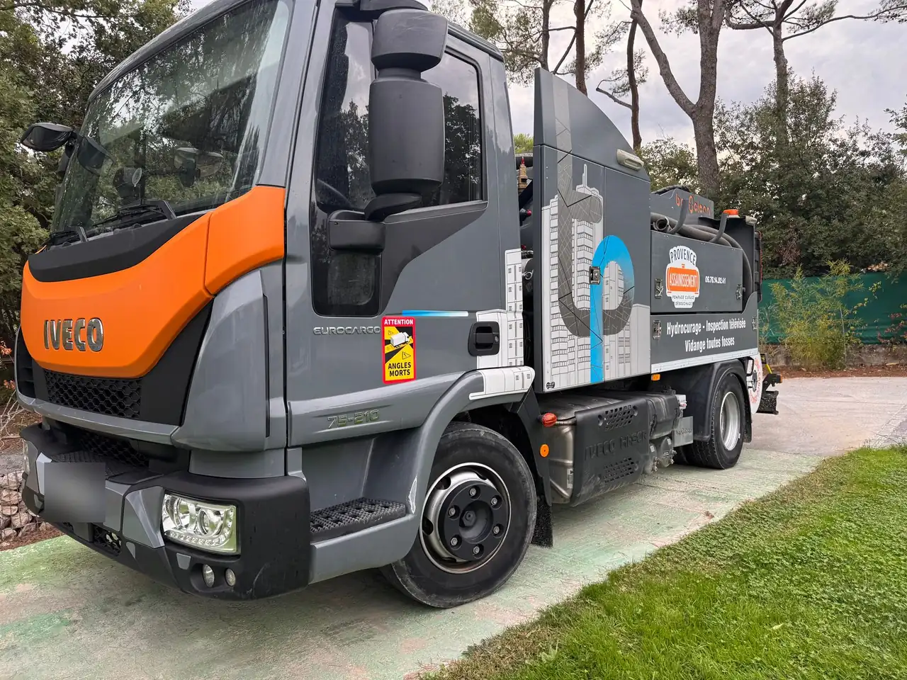 Le camion de Provence Assainissement, cabine orange, garé dans une allée